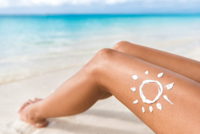 The Care and Feeding of Your Skin woman laying on beach a sun drawn on her leg with sunscreen