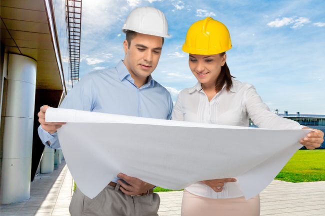 man and woman outside in hard hats looking at construction plans